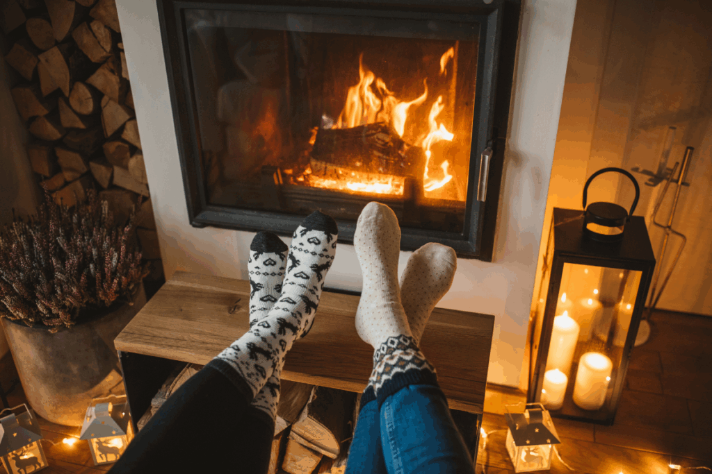 Two people's crossed socked feet on a footrest warming in front of the warmth of a wood burning fire place.
